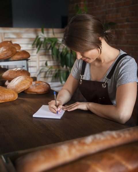 female-baker-taking-notes-while-pastry-shop